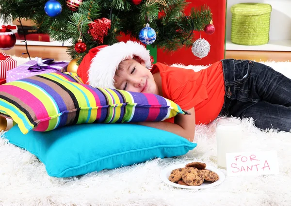 Kleine jongen in Kerstman hoed met melk en koekjes voor santa claus — Stockfoto