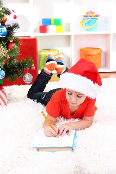 Menino em chapéu de Papai Noel escreve carta para Papai Noel — Fotografia de Stock