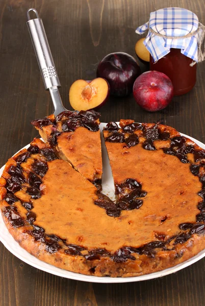 Tasty pie on plate with plums on wooden table — Stock Photo, Image