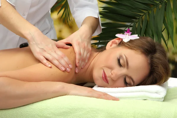 Belle femme dans le salon de spa se faire masser avec des pierres, sur fond de feuilles de palmier — Photo