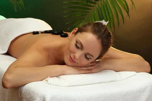 Beautiful young woman in spa salon with spa stones, on green background — Stock Photo, Image
