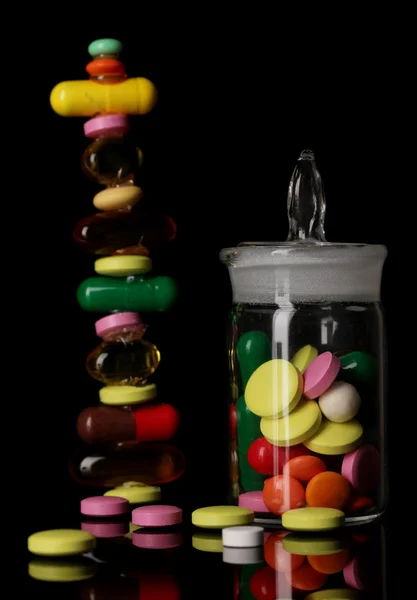 Capsules and pills hill and in receptacle isolated on black — Stock Photo, Image