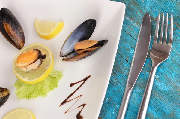 Snack de mejillones y limón en plato sobre mesa de madera azul —  Fotos de Stock