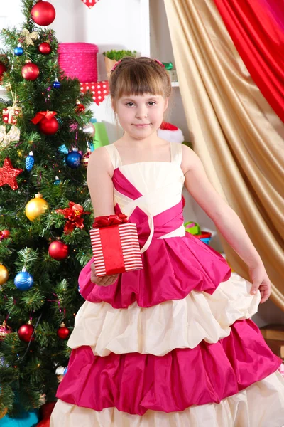 Hermosa niña en vestido de fiesta con regalo en sus manos en la habitación festivamente decorada —  Fotos de Stock