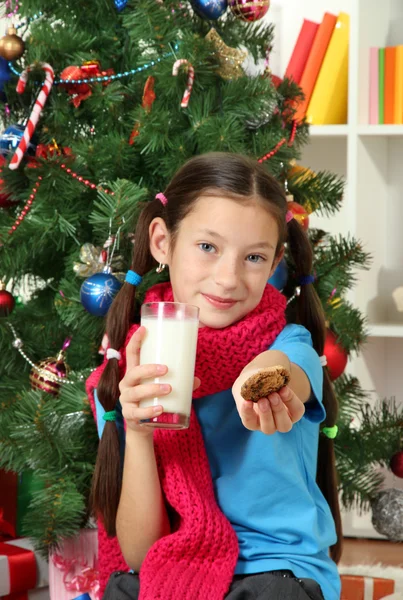 Petite fille avec écharpe rose et verre de lait assis près de l'arbre de Noël — Photo