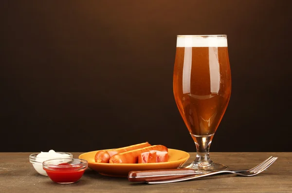 Cerveza y embutidos a la parrilla sobre mesa de madera sobre fondo marrón —  Fotos de Stock