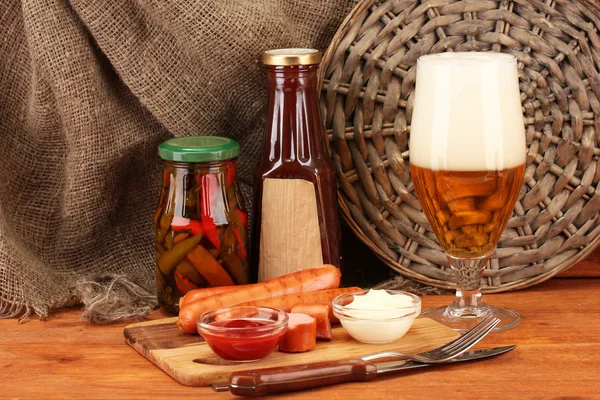 Cerveza y embutidos a la parrilla sobre mesa de madera sobre fondo de saco —  Fotos de Stock