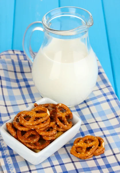 Sabrosos pretzels en tazón blanco y jarra de leche en la mesa de madera de cerca — Foto de Stock