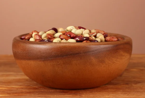 Dřevěná miska s fazolemi na dřevěný stůl na hnědé pozadí — Stock fotografie