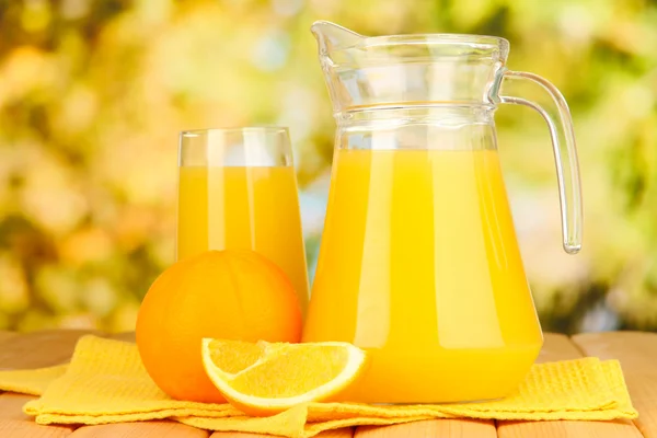 Полный стакан и кувшин апельсинового сока и апельсинов на открытом столе — стоковое фото