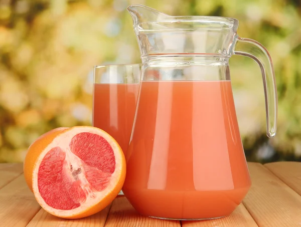 Vol glas en kruik van grapefruitsap en grapefruits op houten tafel buiten — Stockfoto