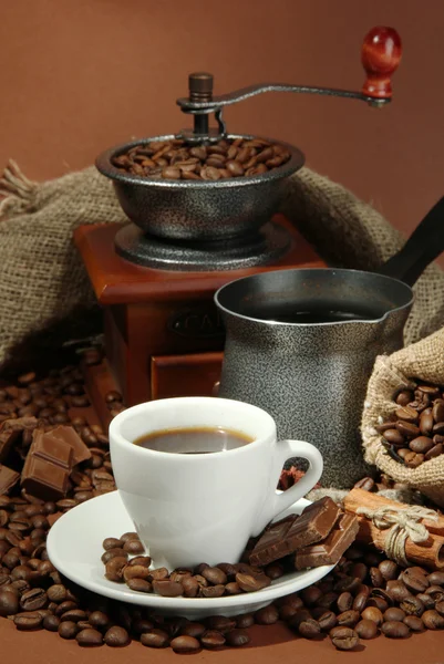 Cup of coffee, grinder, turk and coffee beans on brown background — Stock Photo, Image