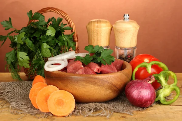 Rå nötkött med örter och kryddor på träbord på brun bakgrund — Stockfoto