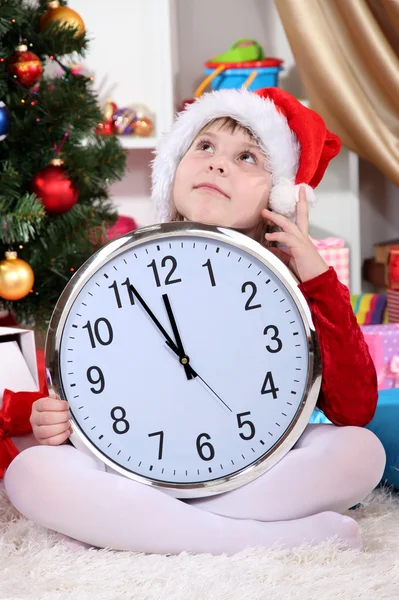 Beautiful little girl with clock in anticipation of New Year in festively decorated room Stock Picture