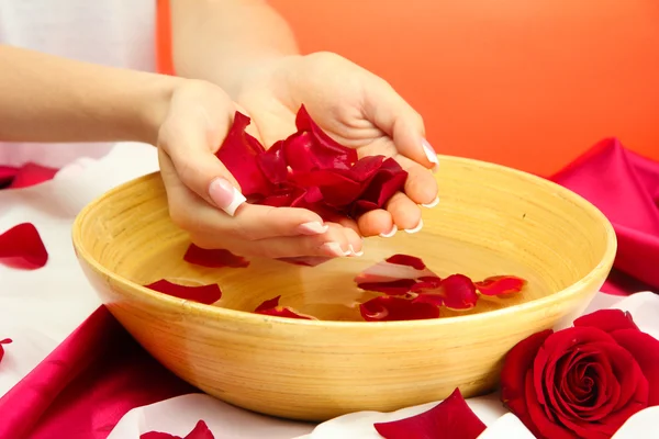 Mani di donna con ciotola di legno di acqua con petali, su sfondo rosso — Foto Stock