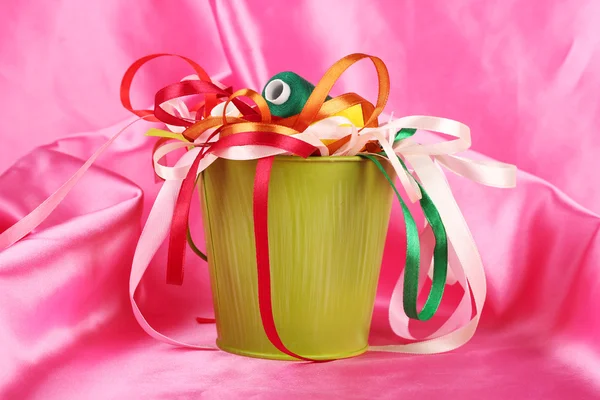 Color bucket with multicolor ribbons and thread on pink fabric background — Stock Photo, Image