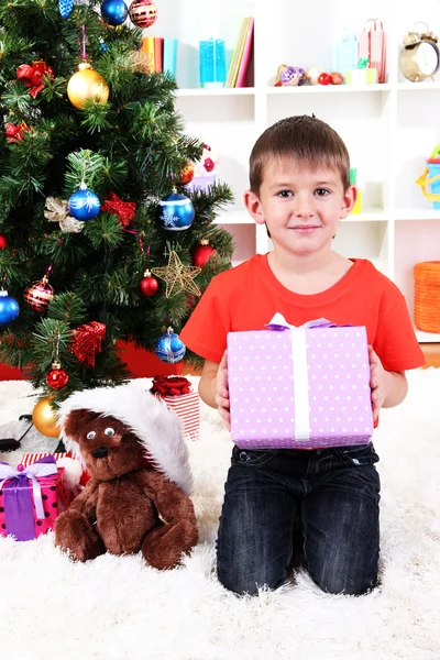 Kleiner Junge sitzt mit Geschenk in der Hand neben Weihnachtsbaum — Stockfoto