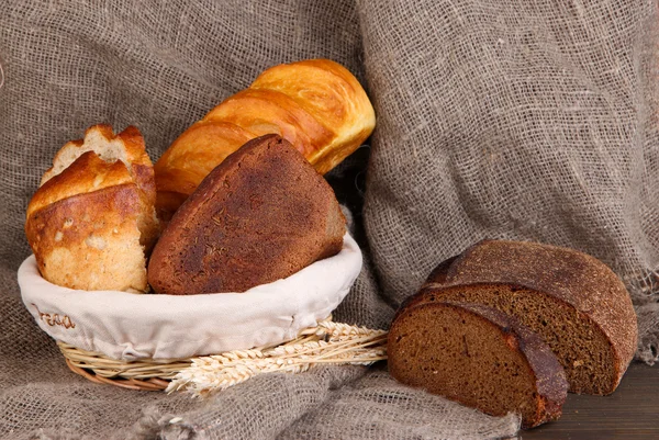 Pane fresco in cesto su tavolo di legno su fondo saccheggiato — Foto Stock