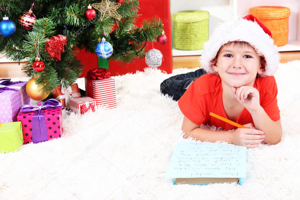 Little boy in Santa hat writes letter to Santa Claus