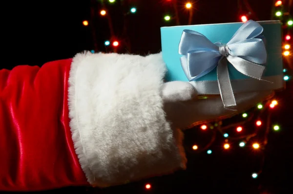 Papai Noel mão segurando caixa de presente no fundo brilhante — Fotografia de Stock