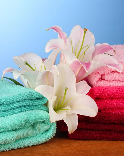 Stack of towels with pink lily on blue background — Stock Photo, Image