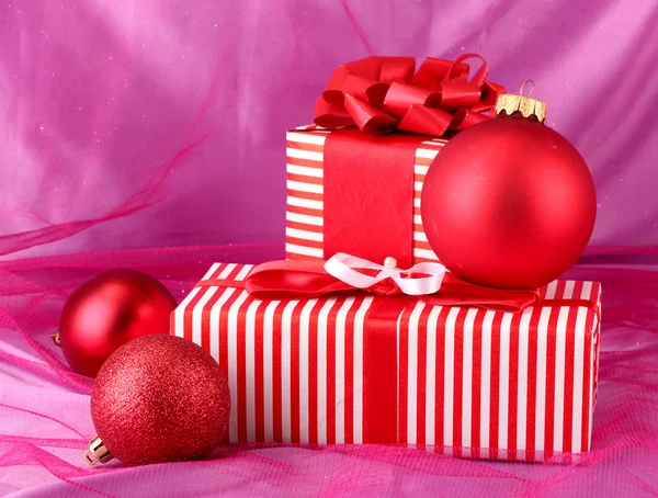 Coloridos regalos rojos con lazo y bolas de Navidad sobre fondo rosa — Foto de Stock