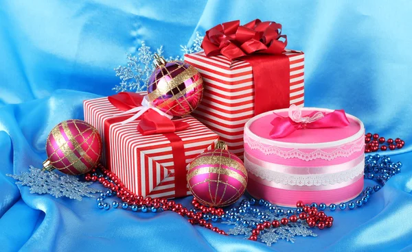 Colorful red and pink gifts with Christmas balls, snowflakes and beads on blue background — Stock Photo, Image