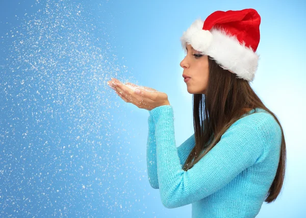 Beautiful young woman blowing snow, on blue background — Stock Photo, Image