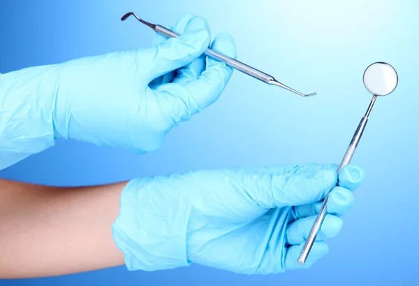 Hände in blauen Handschuhen, die Zahnwerkzeuge auf blauem Hintergrund halten — Stockfoto