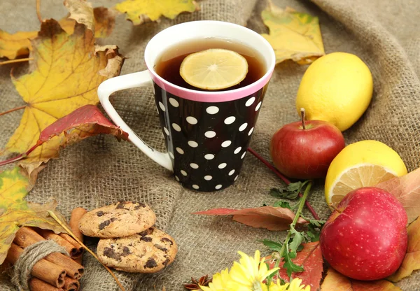 Cup of hot tea and autumn leaves, on burlap background — Stock Photo, Image