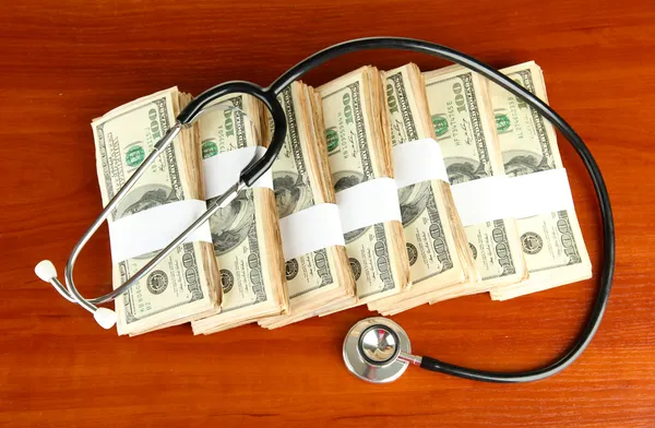 Healthcare cost concept: stethoscope and dollars on wooden background — Stock Photo, Image