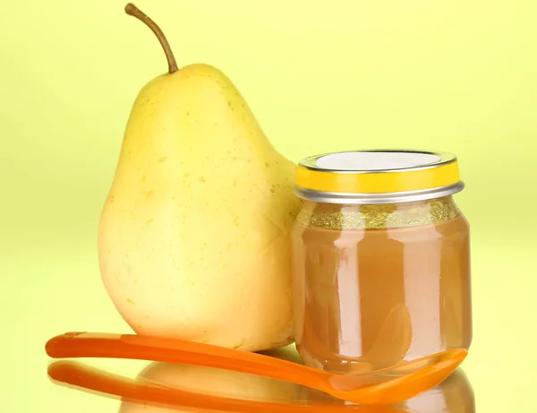 Useful and tasty baby food with pear and spoon on green background — Stock Photo, Image