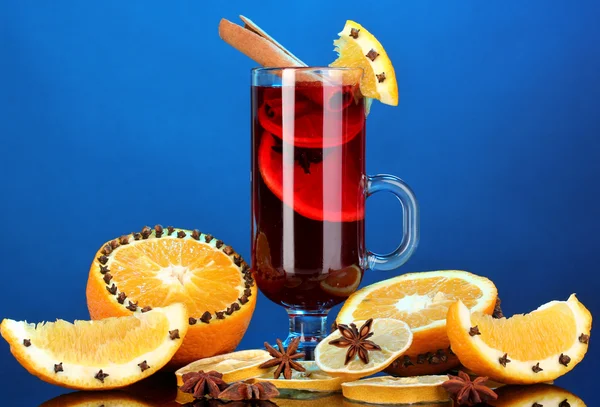 Duftender Glühwein im Glas mit Gewürzen und Orangen auf blauem Hintergrund — Stockfoto