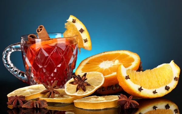 Fragrant mulled wine in glass with spices and oranges around on blue background — Stock Photo, Image