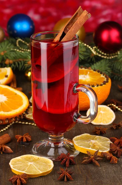 Geurige glühwein in glas met specerijen en sinaasappelen rond op houten tafel op rode achtergrond — Stockfoto