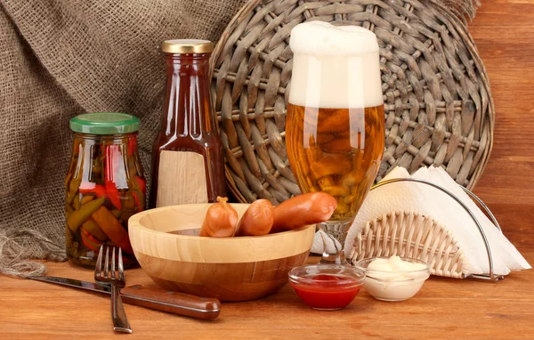 Cerveja e salsichas grelhadas em mesa de madeira sobre fundo de pano de saco — Fotografia de Stock