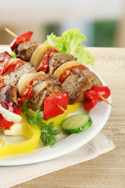 Tasty grilled meat and vegetables on skewer on plate, on wooden table — Stock Photo, Image