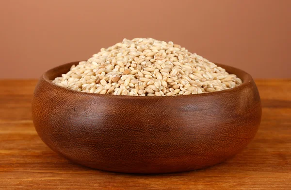 Raw buckwheat in wooden bowl on table on brown background — Stock Photo, Image