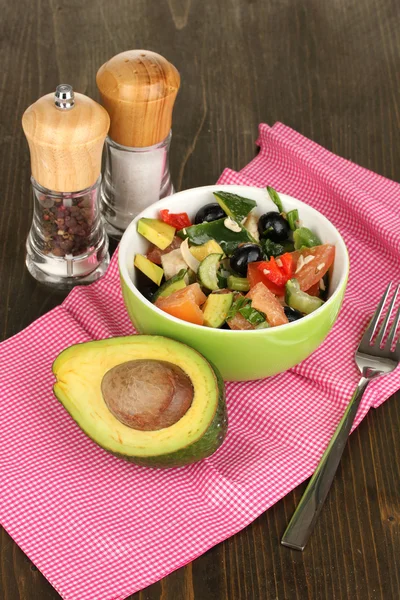 Вкусный салат из авокадо в миске, окруженный специями на деревянном столе крупным планом — стоковое фото