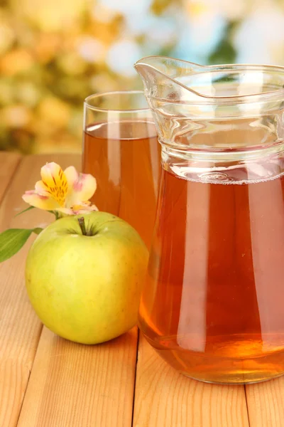 Vol glas en kruik van appelsap en apple op houten tafel buiten — Stockfoto