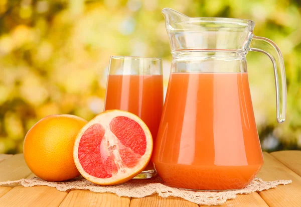 Full glass and jug of grapefruit juice and grapefruits on wooden table outdoor — Stock Photo, Image