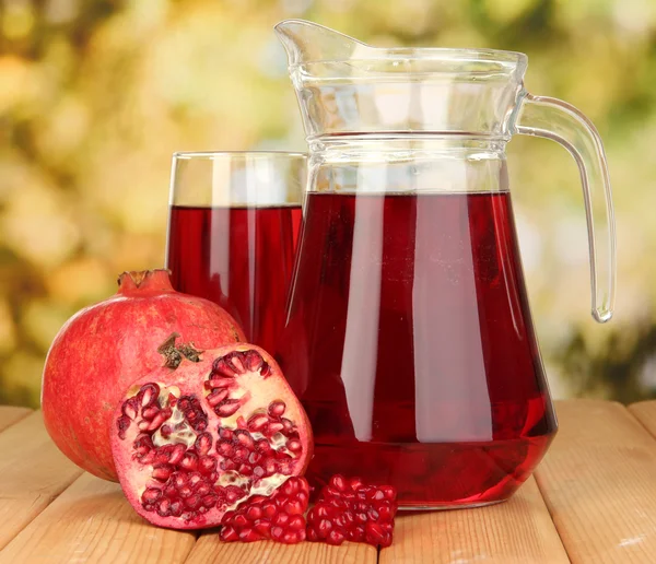 Full glass and jug of pomegranate juice and pomegranate on wooden table outdoor — Stock Photo, Image
