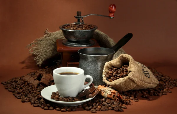 Kopp kaffe, kvarn, turk och kaffebönor på brun bakgrund — Stockfoto