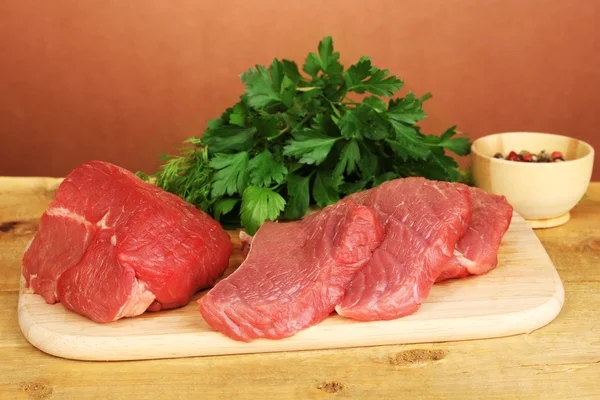 Rå nötkött med kryddor på träbord på brun bakgrund — Stockfoto