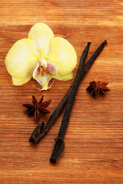 Ванильные стручки и аниса с цветком, на коричневом деревянном фоне — стоковое фото