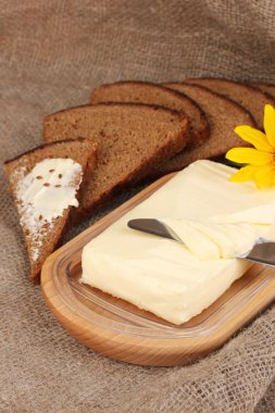 Ahşap kutusunda ekmek ve arka plan çuval bezi üzerinde çiçekler çevrili tereyağı