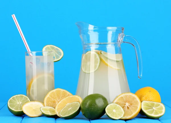 Citrus saft i kannan och glas av citrus runt på träbord på blå bakgrund — Stockfoto