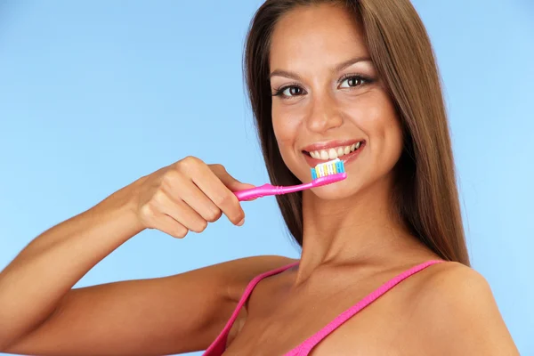 Hermosa joven con cepillo de dientes sobre fondo azul — Foto de Stock