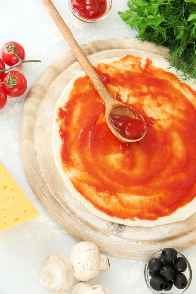 Ciasto do pizzy z sosem pomidorowym na desce na białym tle — Zdjęcie stockowe