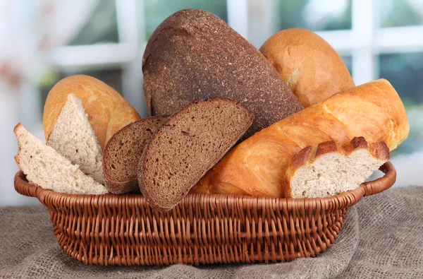 Świeże pieczywo w kosz na drewnianym stole na tle okna — Zdjęcie stockowe